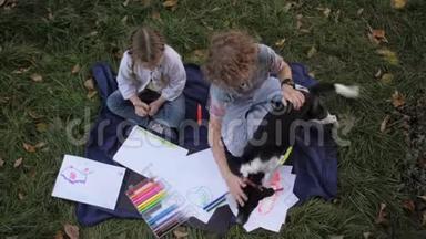 两个快乐的孩子，男孩和女孩躺在草地上，夏天公园里带着狗。 孩子们的兄弟姐妹会读书画画，玩游戏
